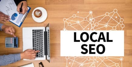 Multiple people are working at a desk. On the desk, there is a cup of coffee, a clipboard with data on it, a calculator, a laptop, a pair of glasses, and an open notebook. There is a graphic to the right that reads "Local SEO"