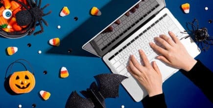 Laptop surrounded by Halloween candy, pumpkins, and bats on a blue background