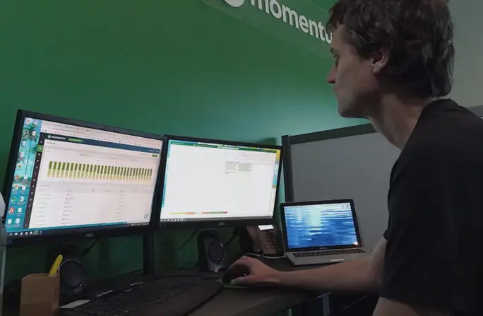 Man analyzing data on multiple computer screens in an office setting.