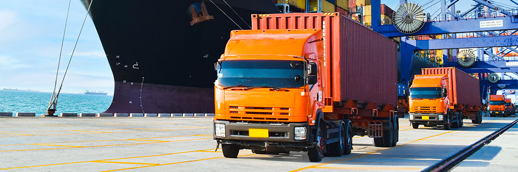 Container shipping, orange color truckload with a container at a harbor. Container port terminal, container delivery.