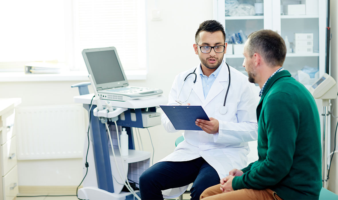 Middle-aged bearded patient having consultation with highly professional physician at modern office, they discussing diagnosis and possible treatment