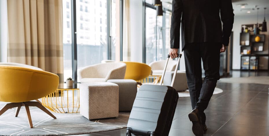 Cropped photo of caucasian businessman wearing suit walking with suitcase in hotel lobby