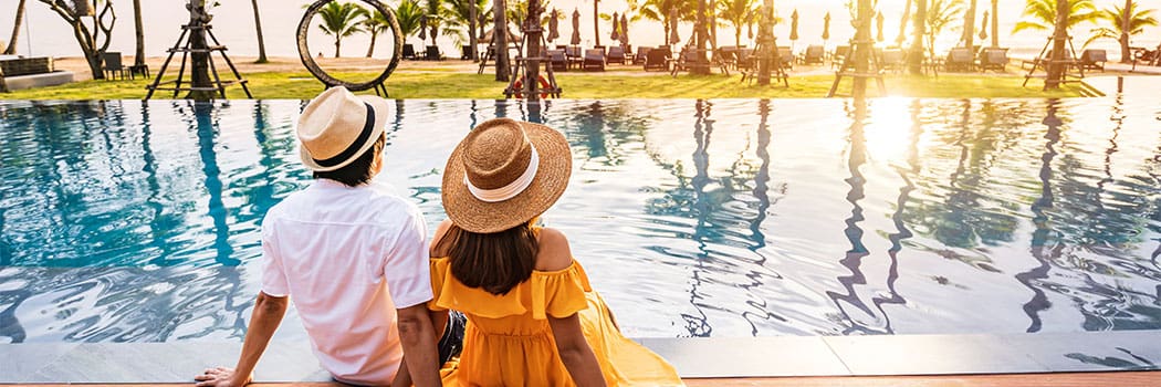 Young couple traveler relaxing and enjoying the sunset by a tropical resort pool while traveling for summer vacation
