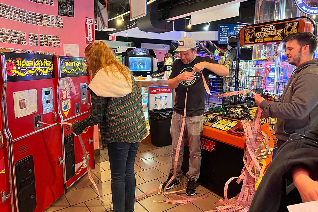 People counting arcade tickets at a redemption center in a lively game arcade.