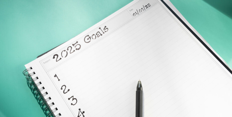 A spiral bound notebook with a pen placed on top of it. The open page of the notebook says '2025 Goals' with a numbered list.